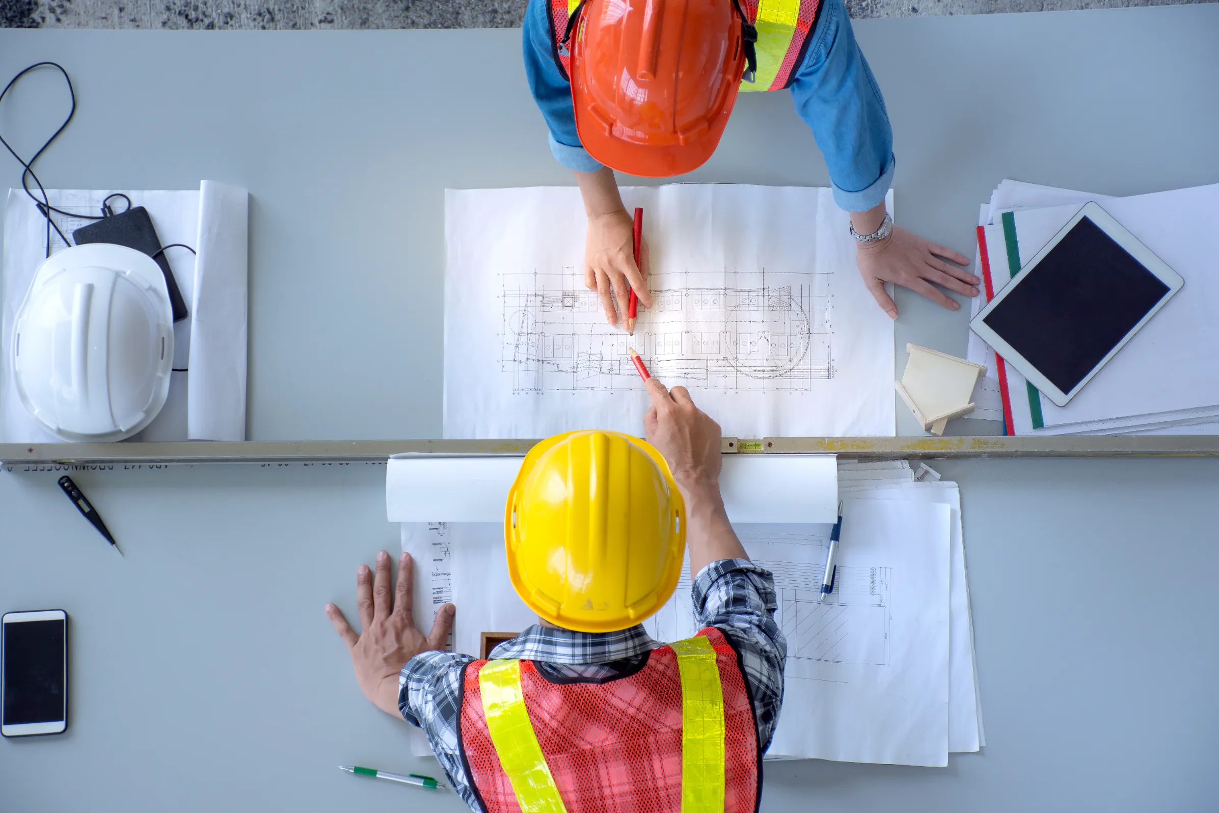 A project manager collaborates with engineers in a bright meeting room, reviewing site maps and construction drawings—highlighting Jewett Construction’s early-stage planning process focused on strategic execution and cost control.