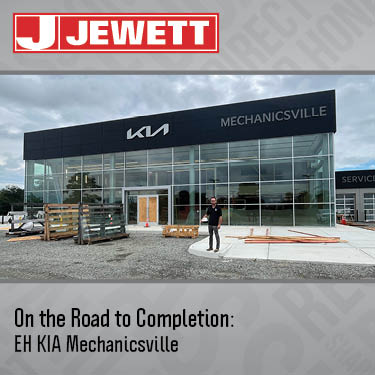 Construction progress at EH KIA Mechanicsville dealership, showing the nearly completed glass-front building with a Jewett Construction superintendent standing in front.