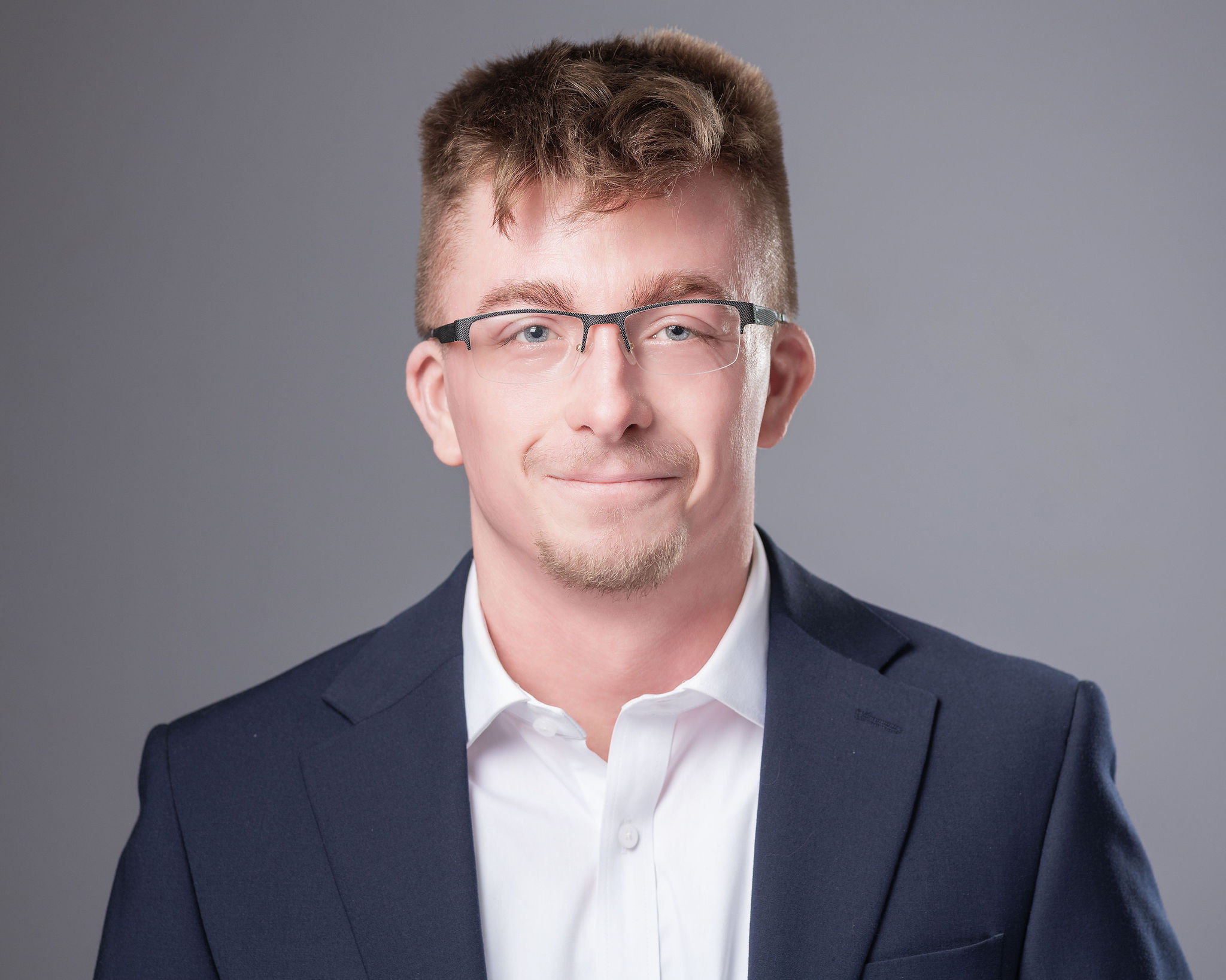 Professional headshot of Doug Reymore, Planning & Development Manager at Jewett Construction, wearing a navy suit and glasses, smiling. He leads risk management, permitting, and site due diligence.
