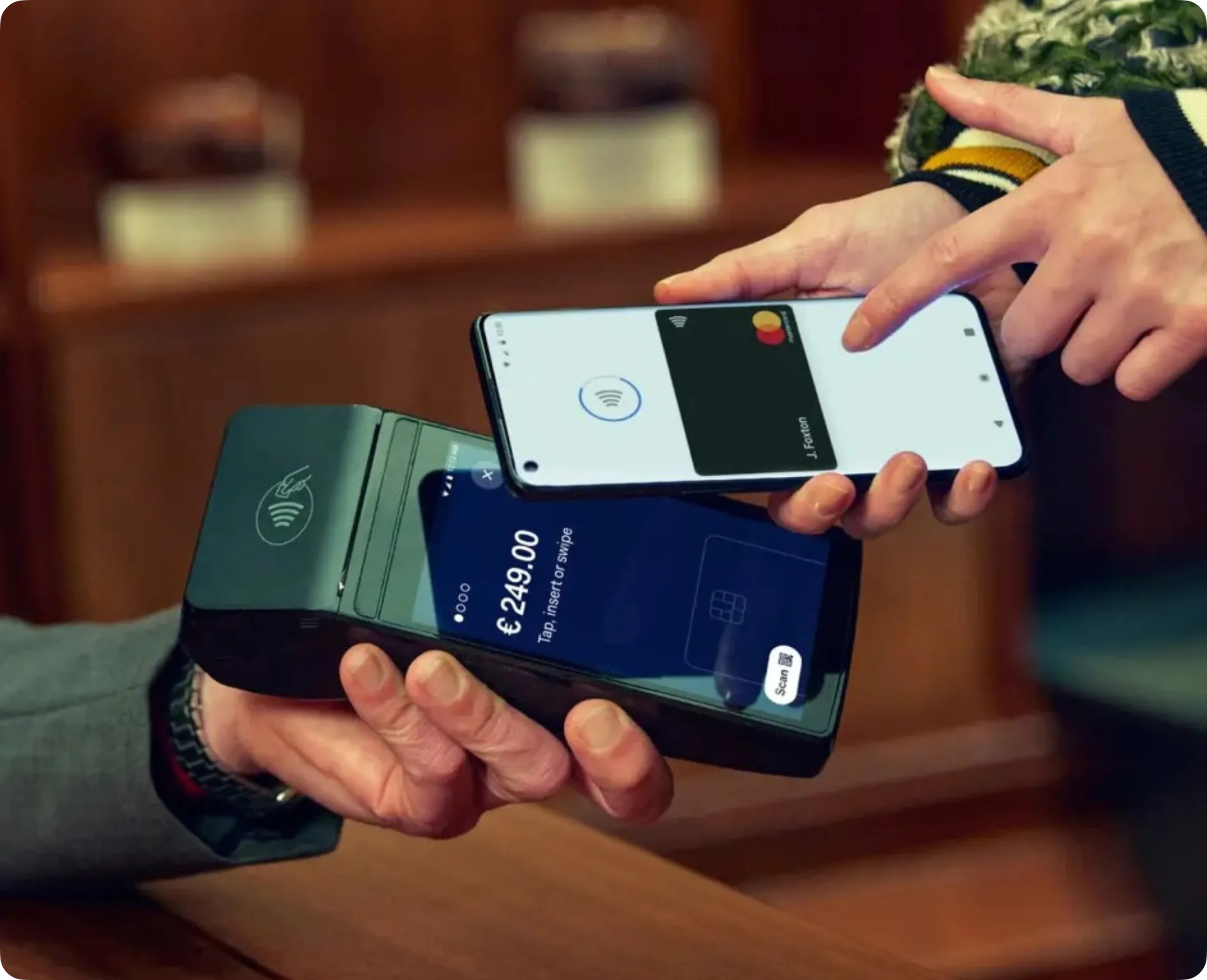 Personne effectuant un paiement sans contact avec un smartphone sur un terminal de paiement affichant 249,00 €.