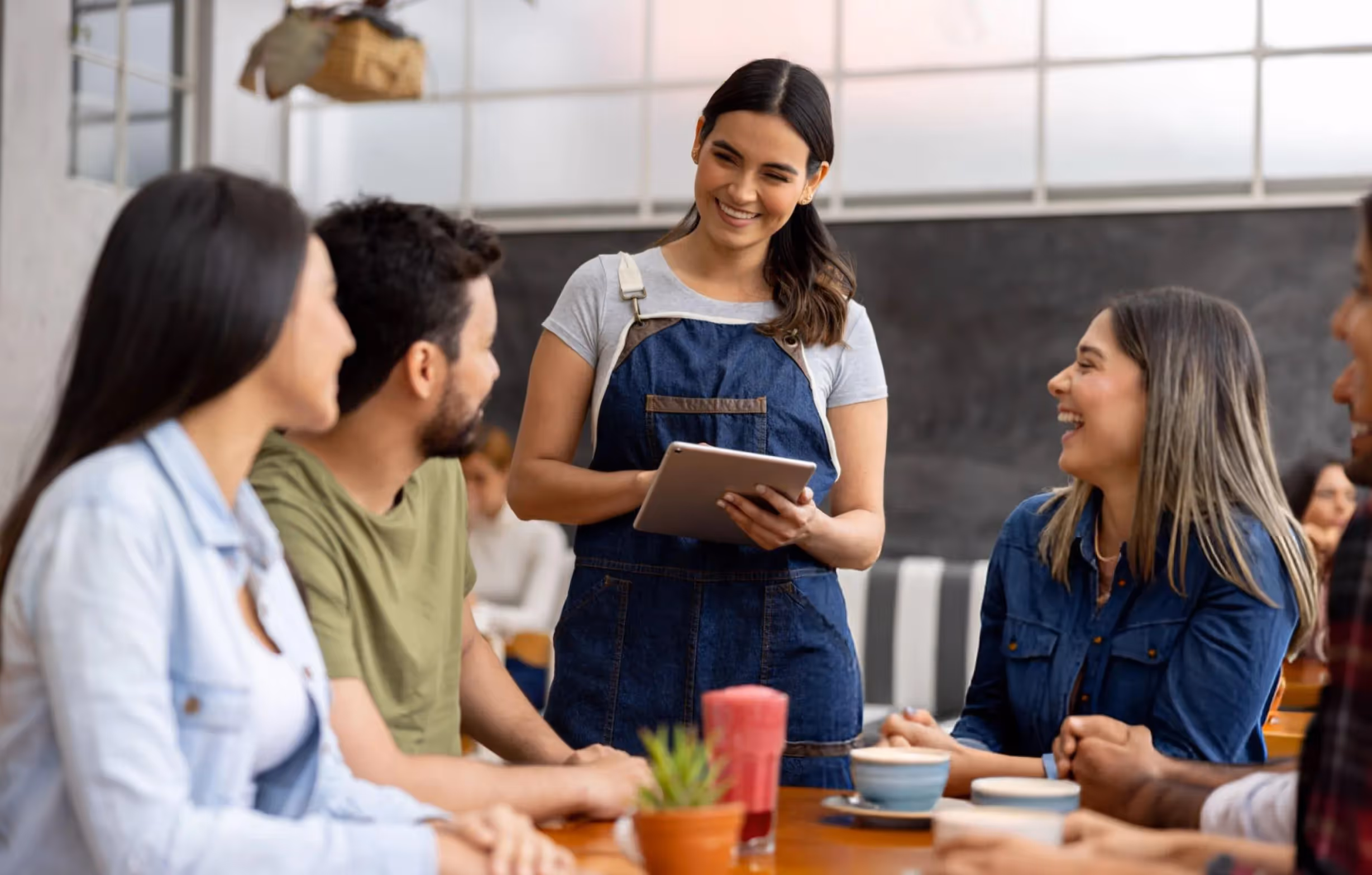 Serveuse souriante avec une tablette prenant une commande de quatre clients assis à une table dans un café.