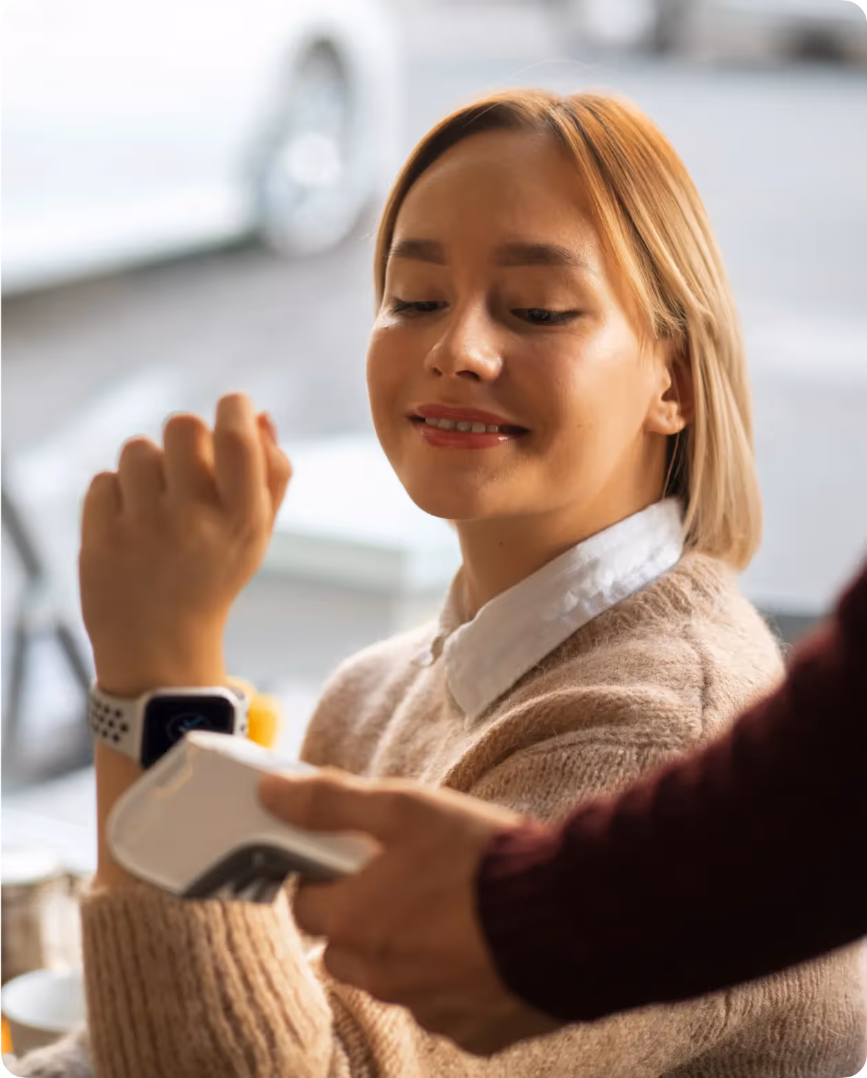 Une femme souriante utilisant une montre connectée pour un paiement sans contact avec un terminal de paiement.