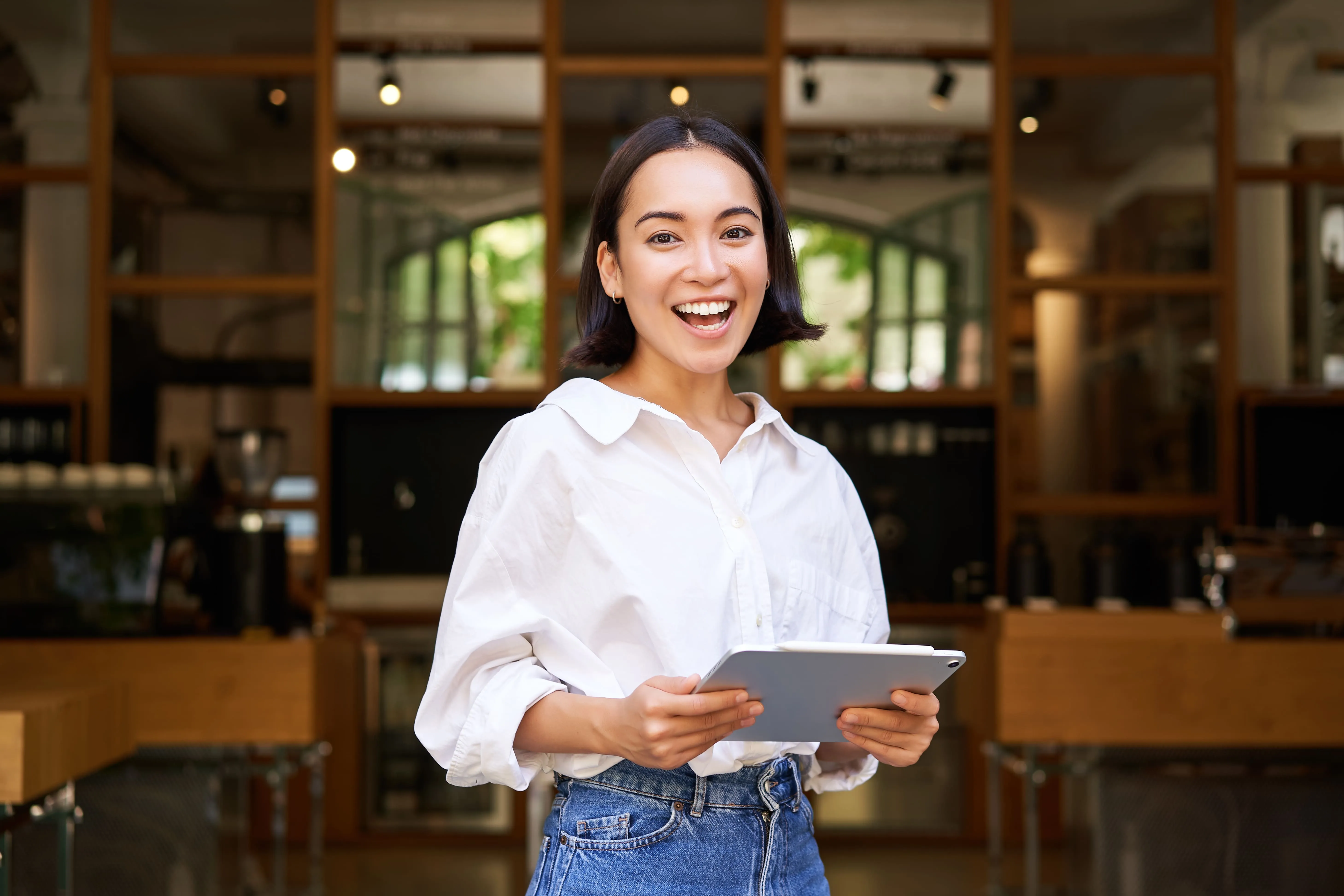 Jeune femme souriante tenant une tablette dans un café moderne au décor en bois.