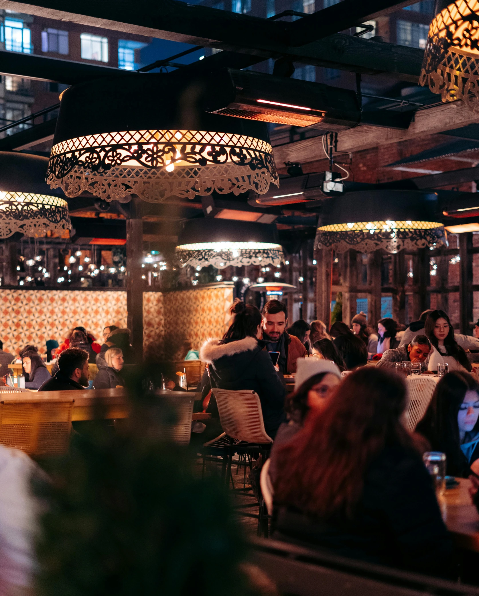Restaurant intérieur animé avec des clients assis sous des luminaires décoratifs chaleureux en soirée.