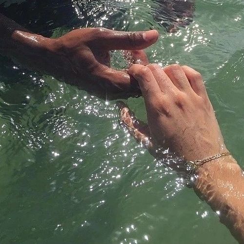 Two people reaching for eachothers hands in the water