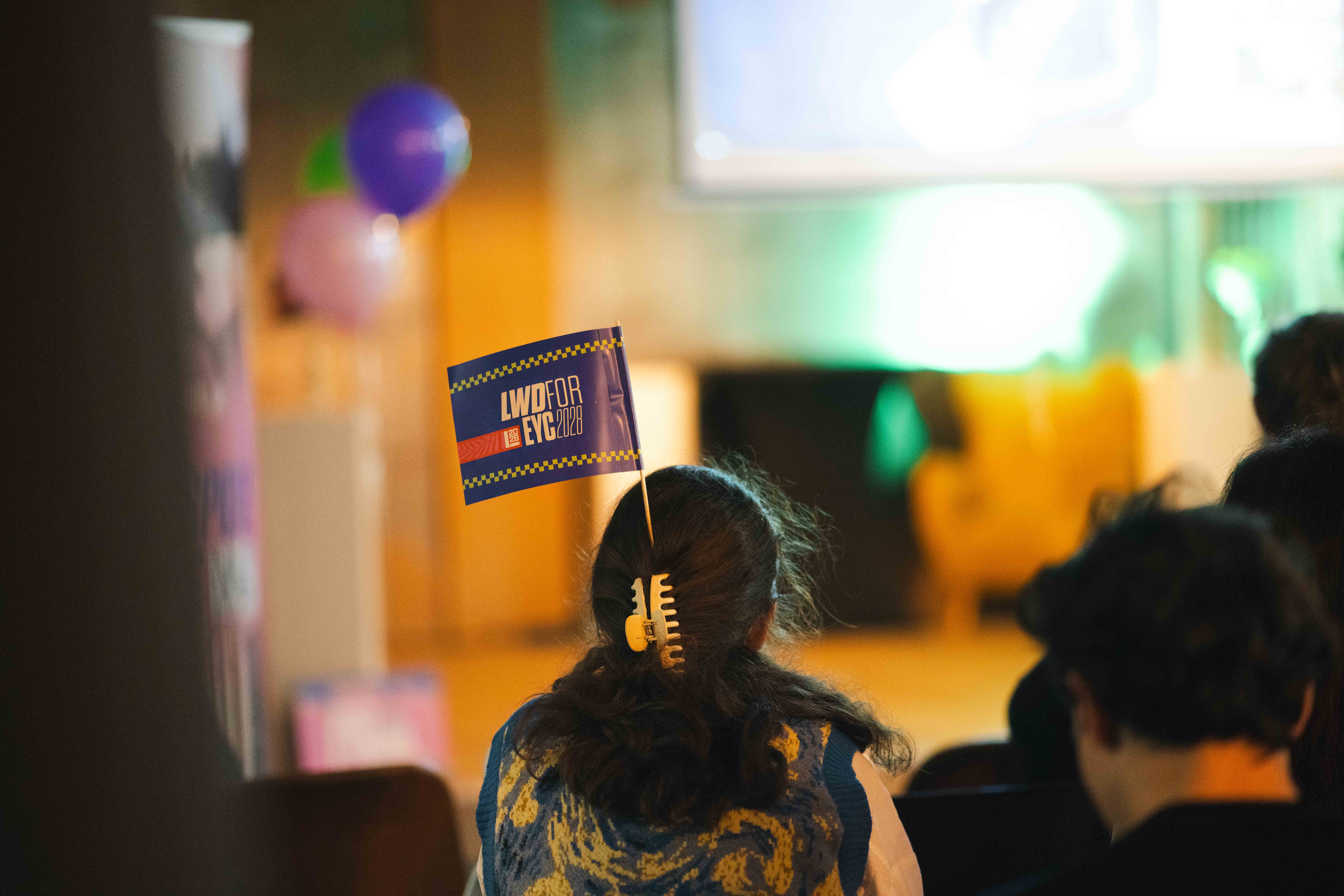 Meisje in publiek met LWD for EYC 2028-vlag in haar haar.