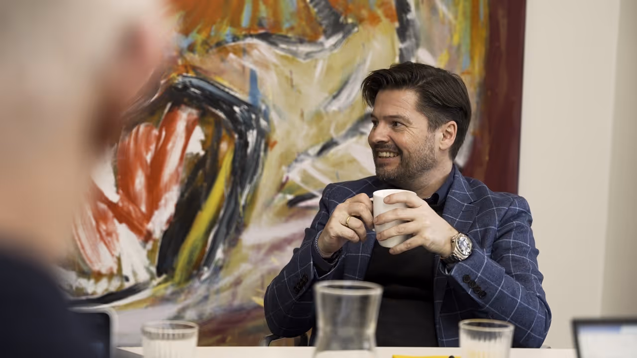 En mand sidder ved et bord med en kop kaffe, omgivet af en rolig og indbydende atmosfære.