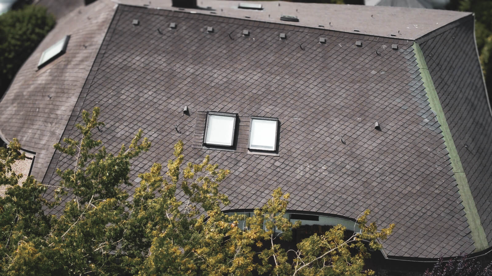 Dacheindeckung mit Bitumenschindel mit Dachfenster und Hagelschaden, Dach wurde oft provisorisch abgedichtet