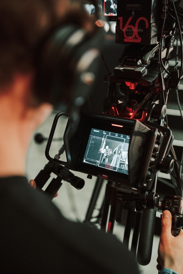 Operator with headphones adjusting a professional video camera displaying a black and white scene on its screen.