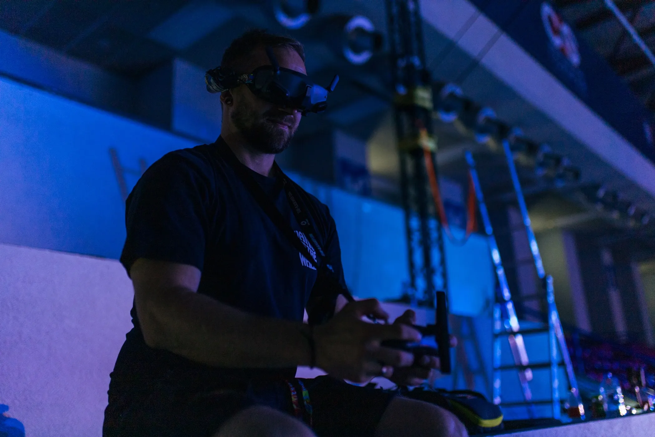 Mężczyzna noszący okulary VR siedzi i trzyma kontroler w ciemnym, niebiesko oświetlonym otoczeniu.