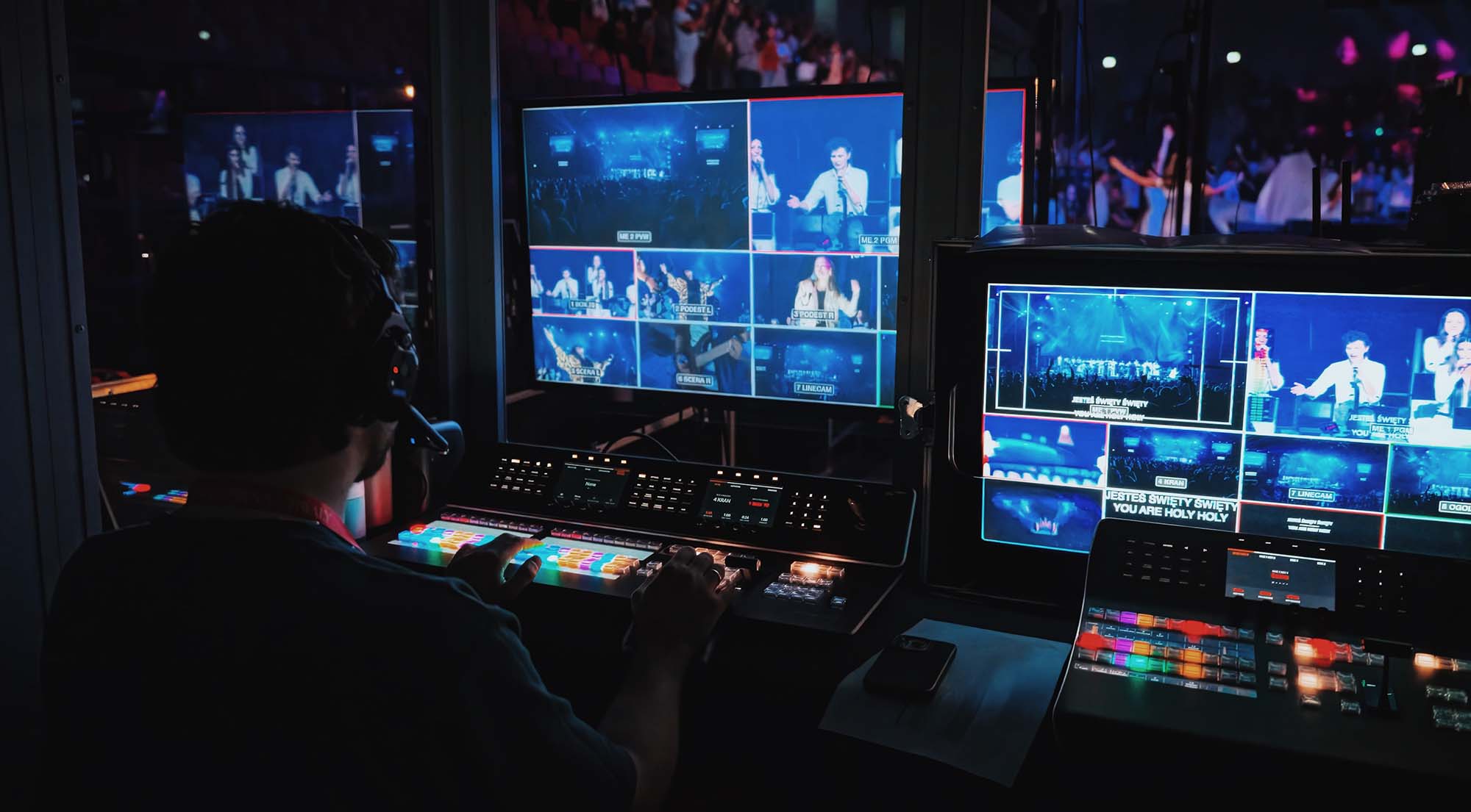 Osoba obsługująca sprzęt do transmisji na żywo z wieloma ekranami pokazującymi różne ujęcia sceny i publiczności podczas wydarzenia na Arenie.