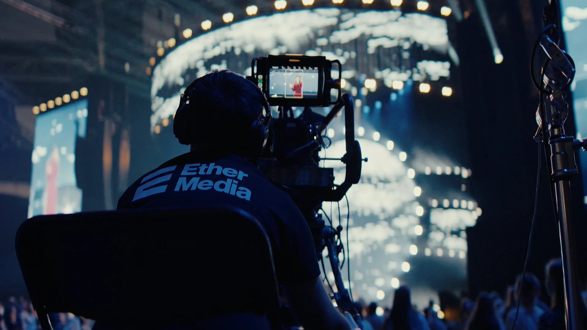 Operator kamera filmujący występ artysty na scenie podczas koncertu z jasnymi, rozmytymi światłami w tle.