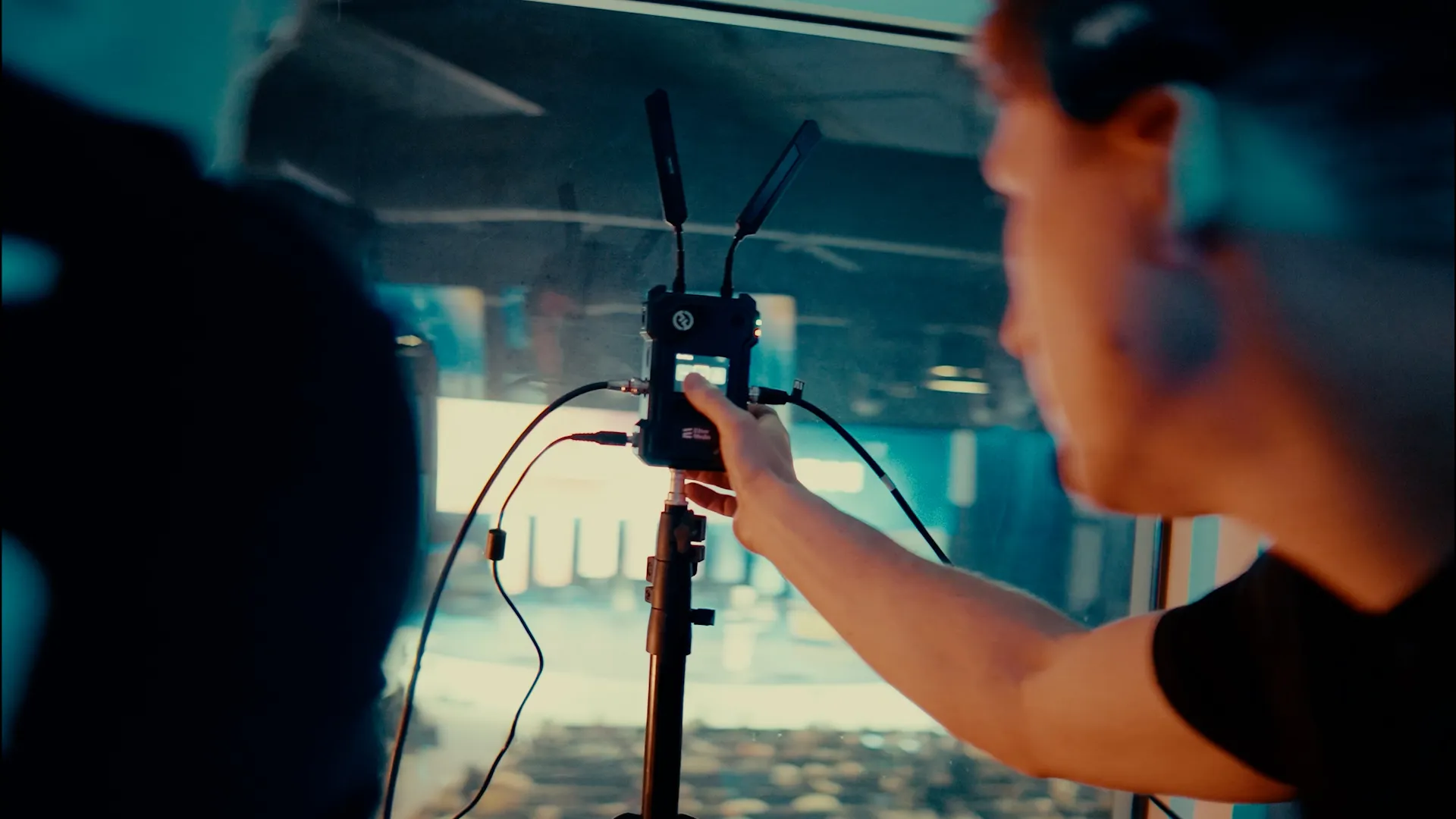 Osoba ustawiająca urządzenie elektroniczne z antenami na statywie przy oknie.