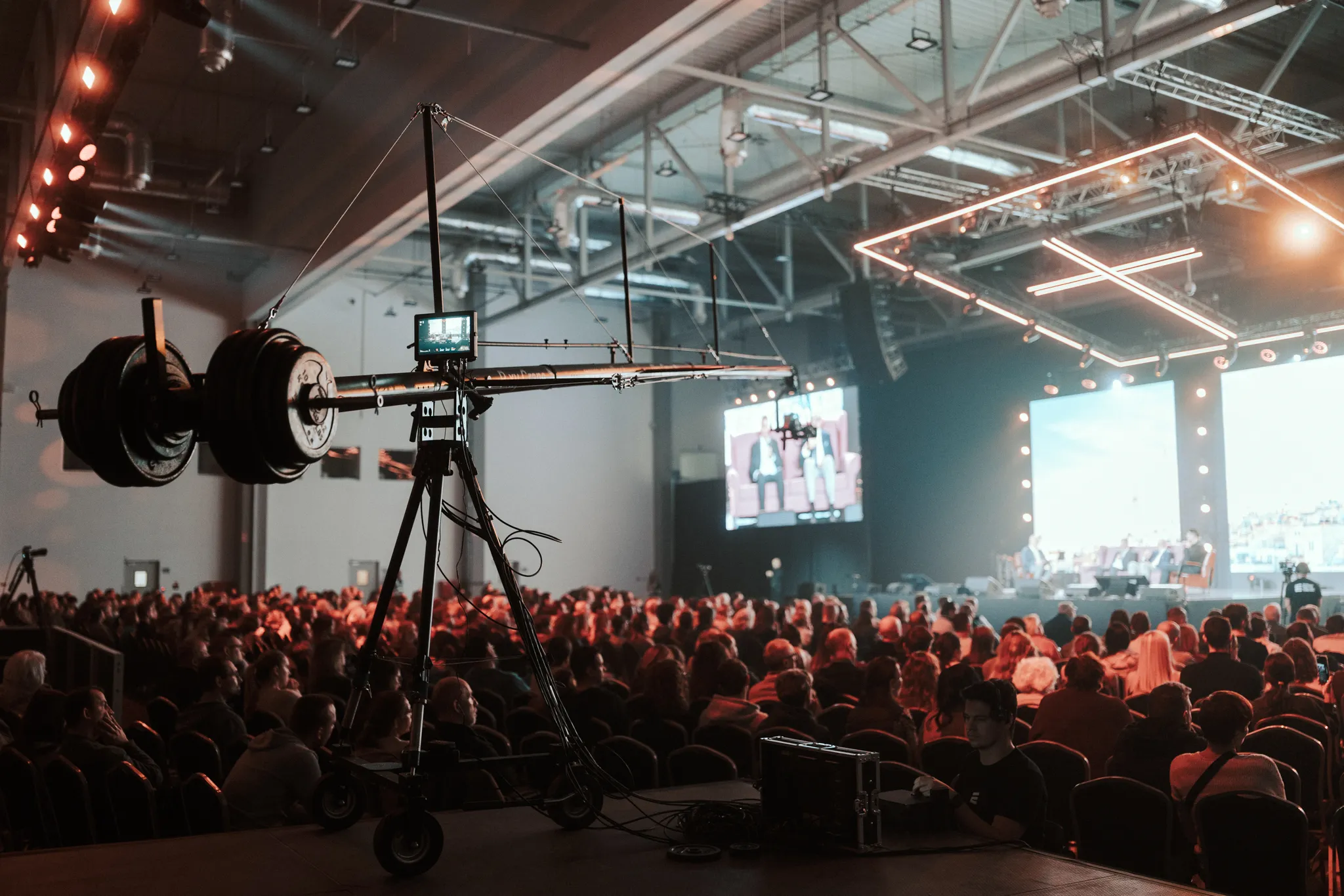 Conference hall with audience seated and a large camera crane capturing a panel discussion on stage.
