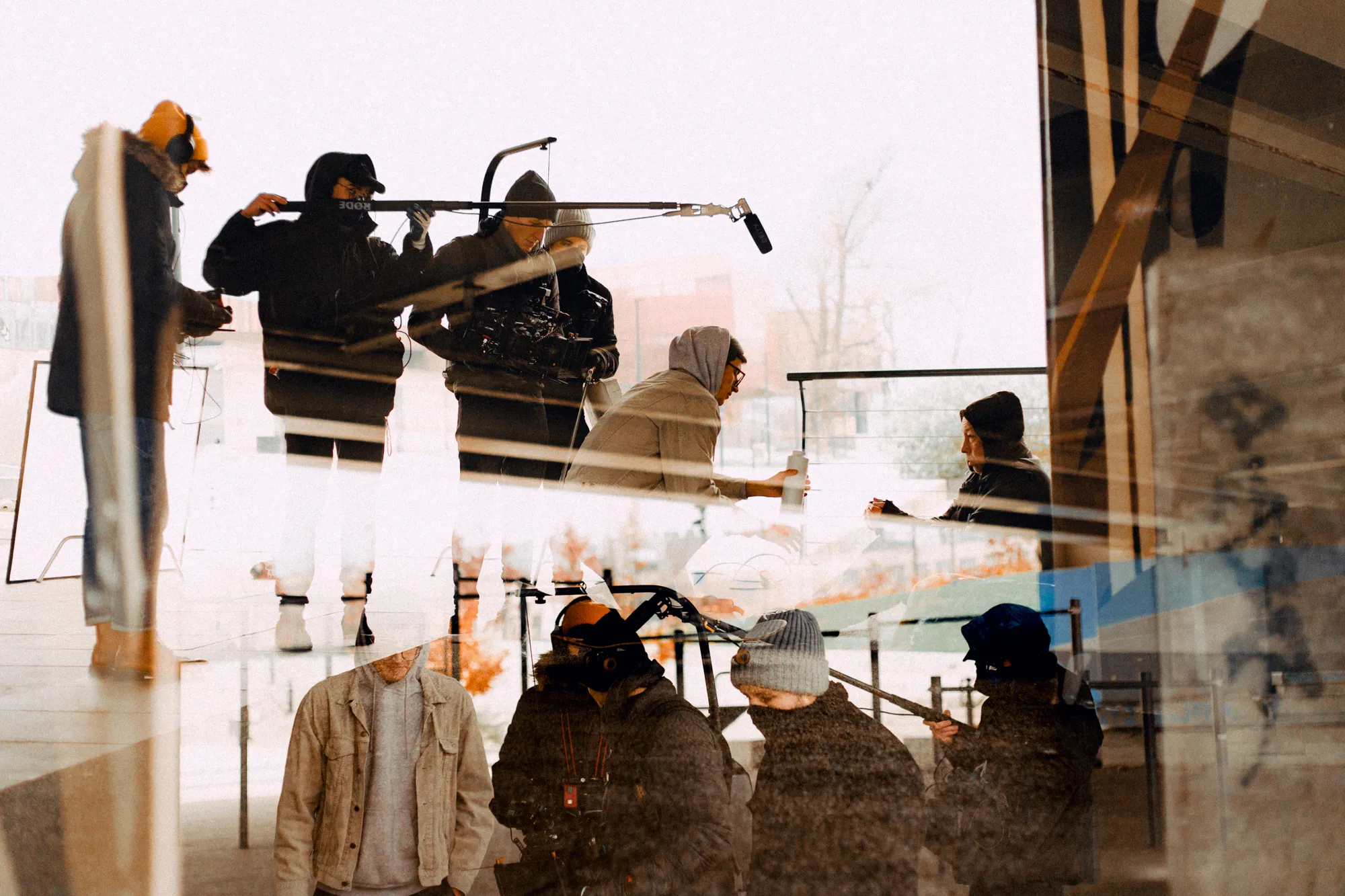 Multiple reflections of a film crew with camera, boom microphone, and people in winter clothing communicating outdoors.