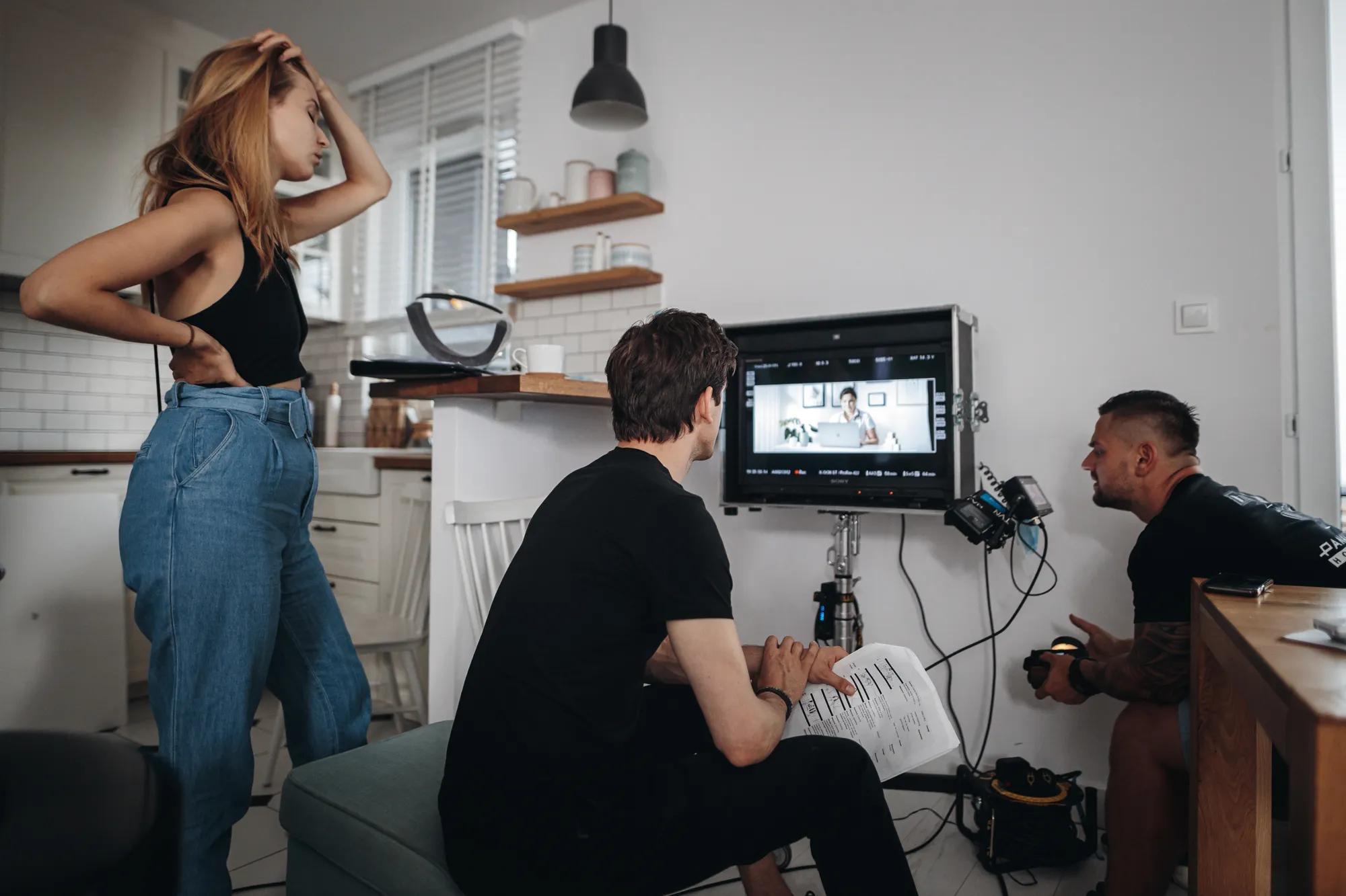 Trzech osób pracujących nad nagraniem w kuchni z monitorem wyświetlającym kobietę przy laptopie.