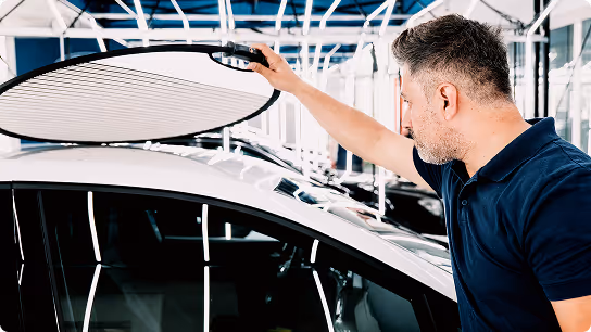 Man adjusting a car roof reflector or diffuser inside a photography studio or showroom.