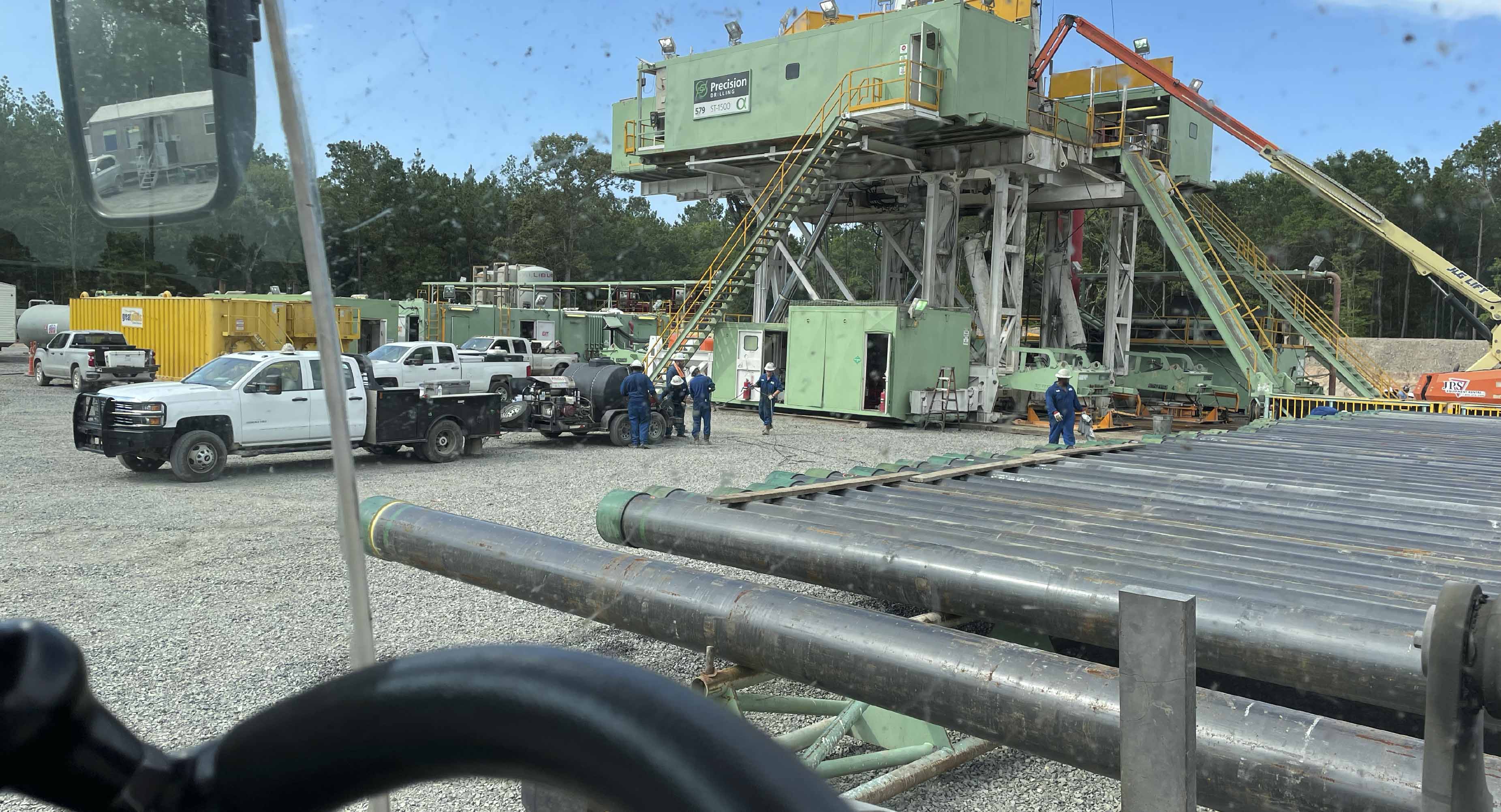 Oilfield workers and service trucks at active drilling rig site in North Louisiana with stacked drill pipe and support equipment for logistics and operations

