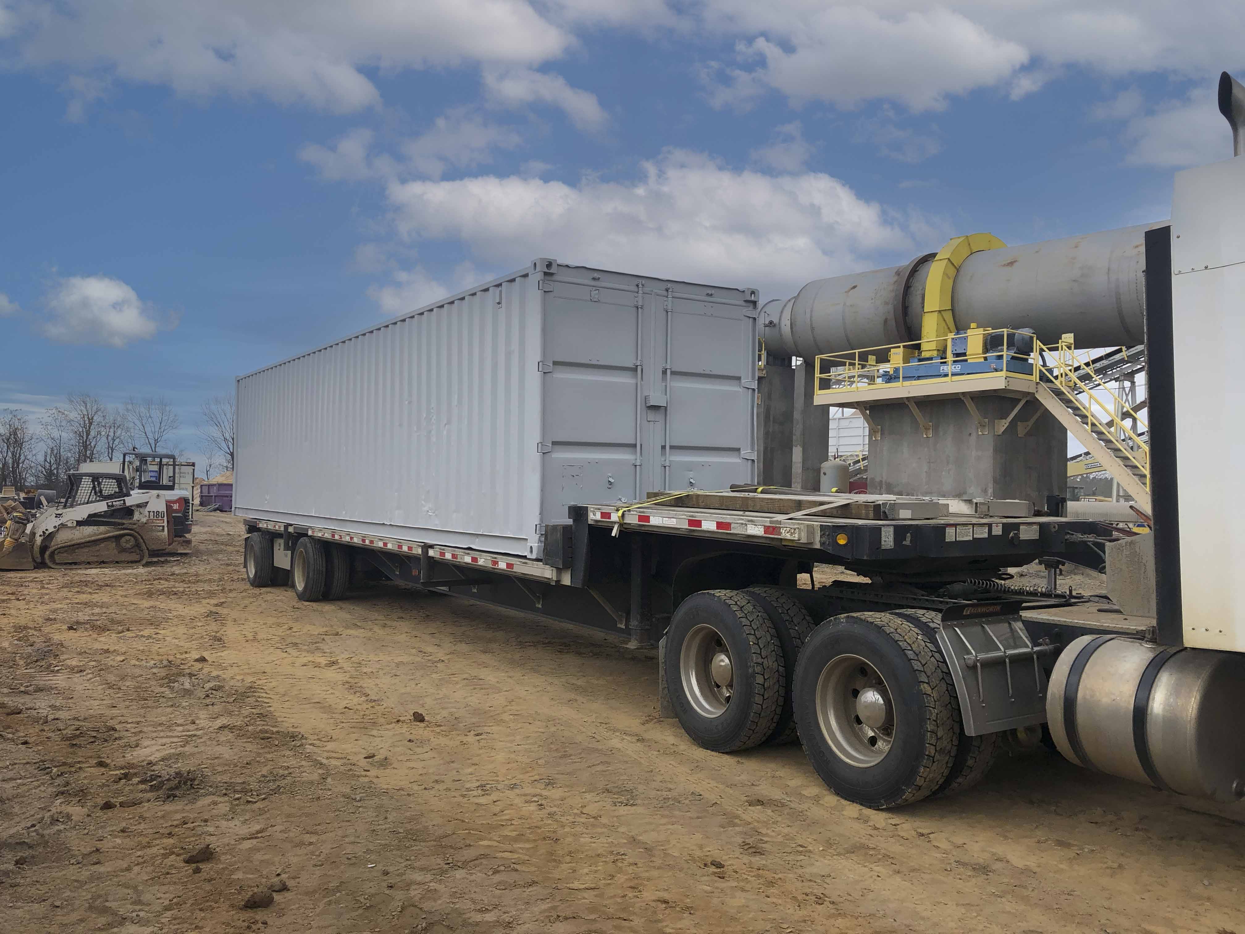 Flatbed truck transporting shipping container at oilfield logistics site in North Louisiana