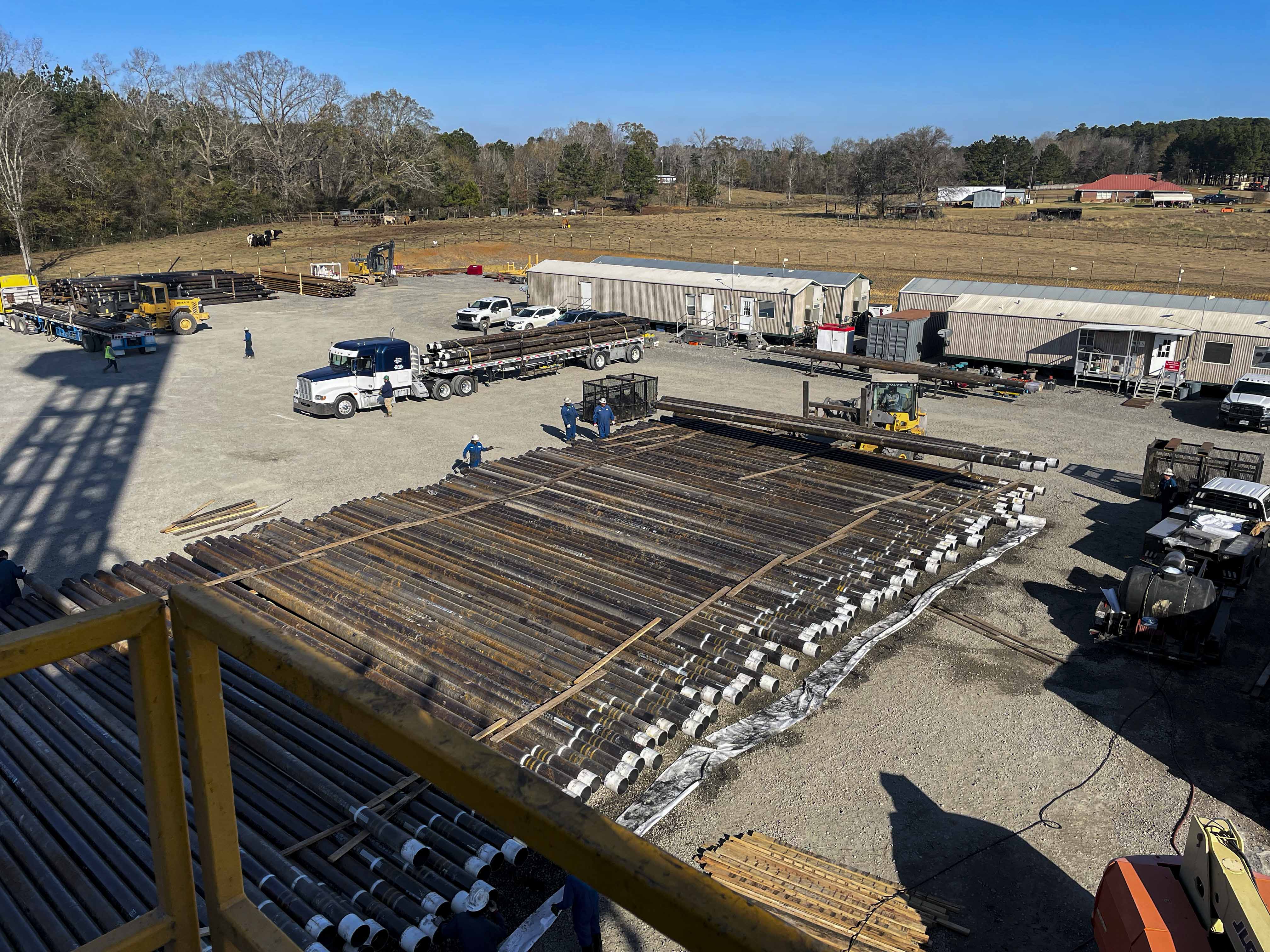 Overhead view of oilfield logistics yard in South Arkansas with stacked drill pipe and transport trucks