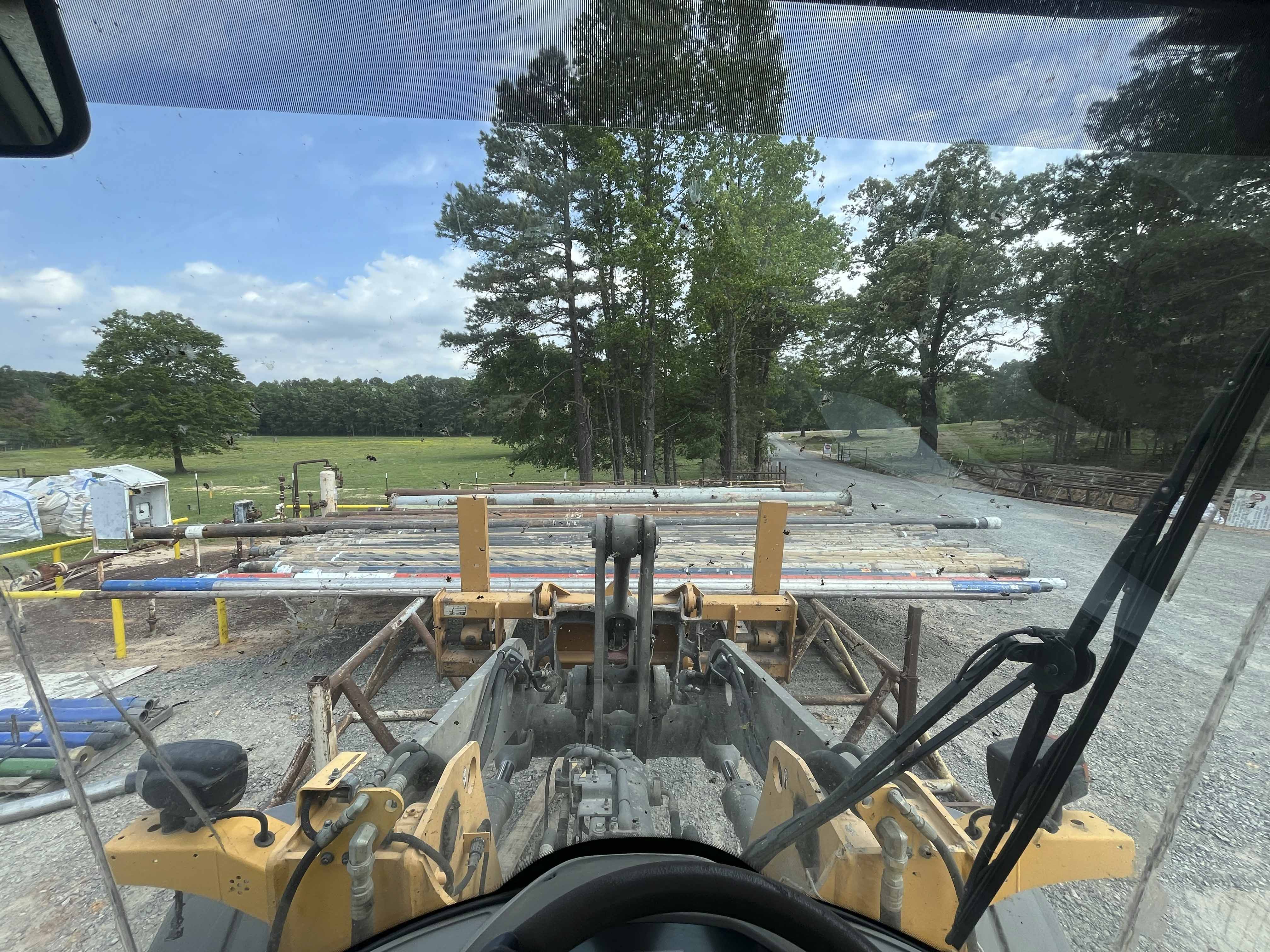 Loader view transporting drill pipe at rural oilfield support site in North Louisiana, providing logistics and pipe handling services