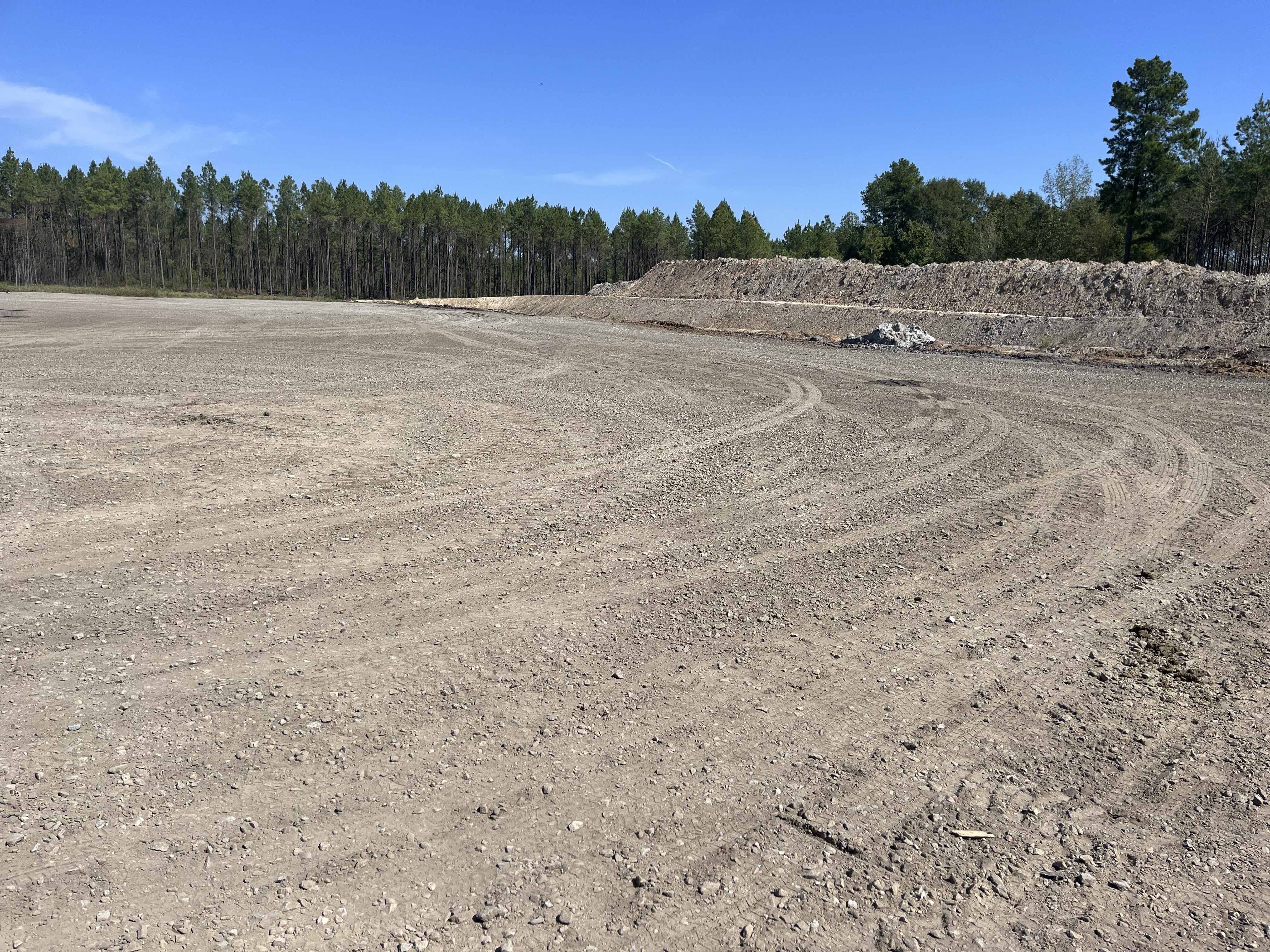 Cleared and graded gravel oilfield site in North Louisiana prepared for equipment staging and drilling operations, with work trucks visible on location