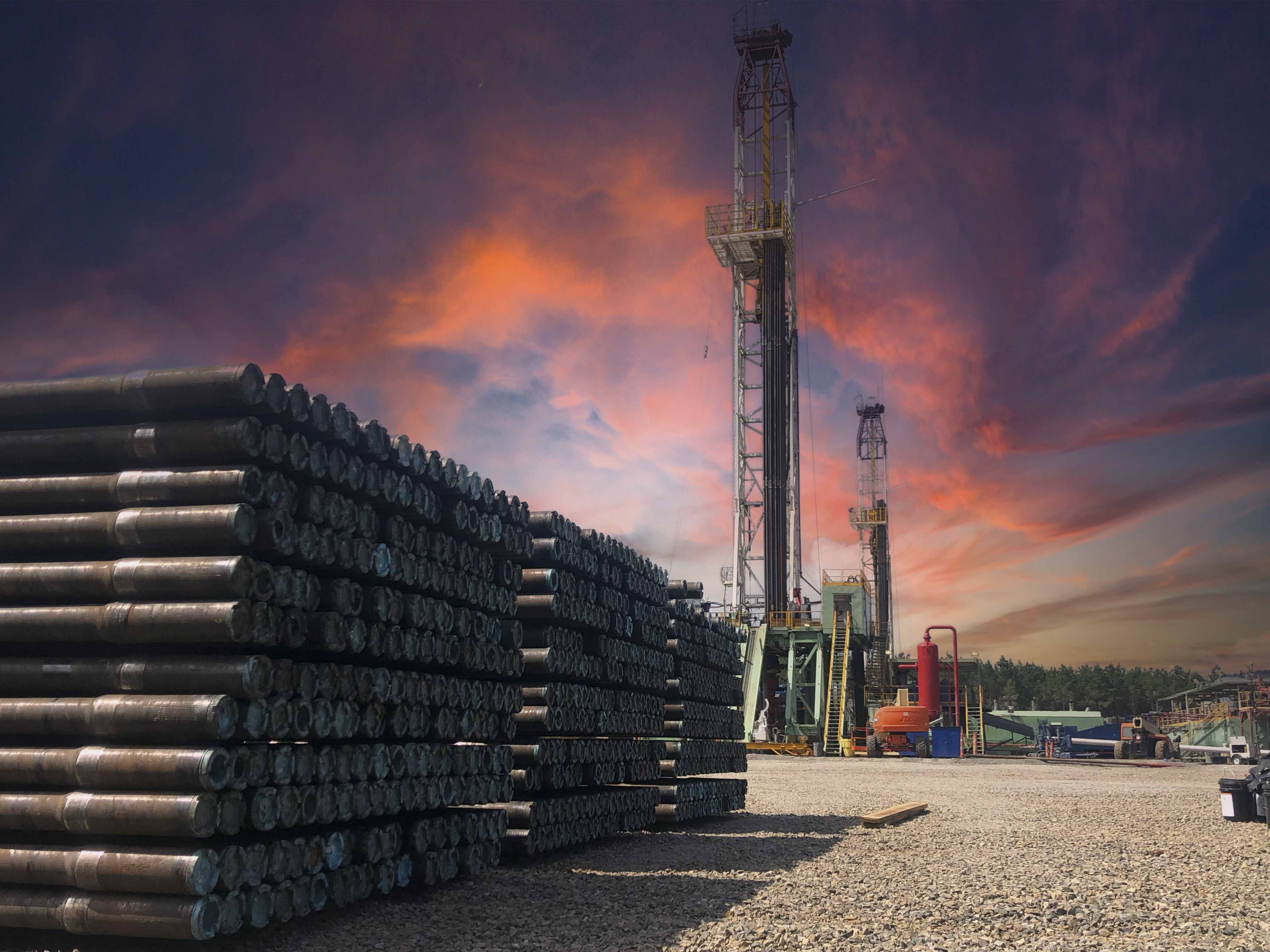 Oilfield drilling rig and stacked pipe under dramatic sunset sky in North Louisiana
