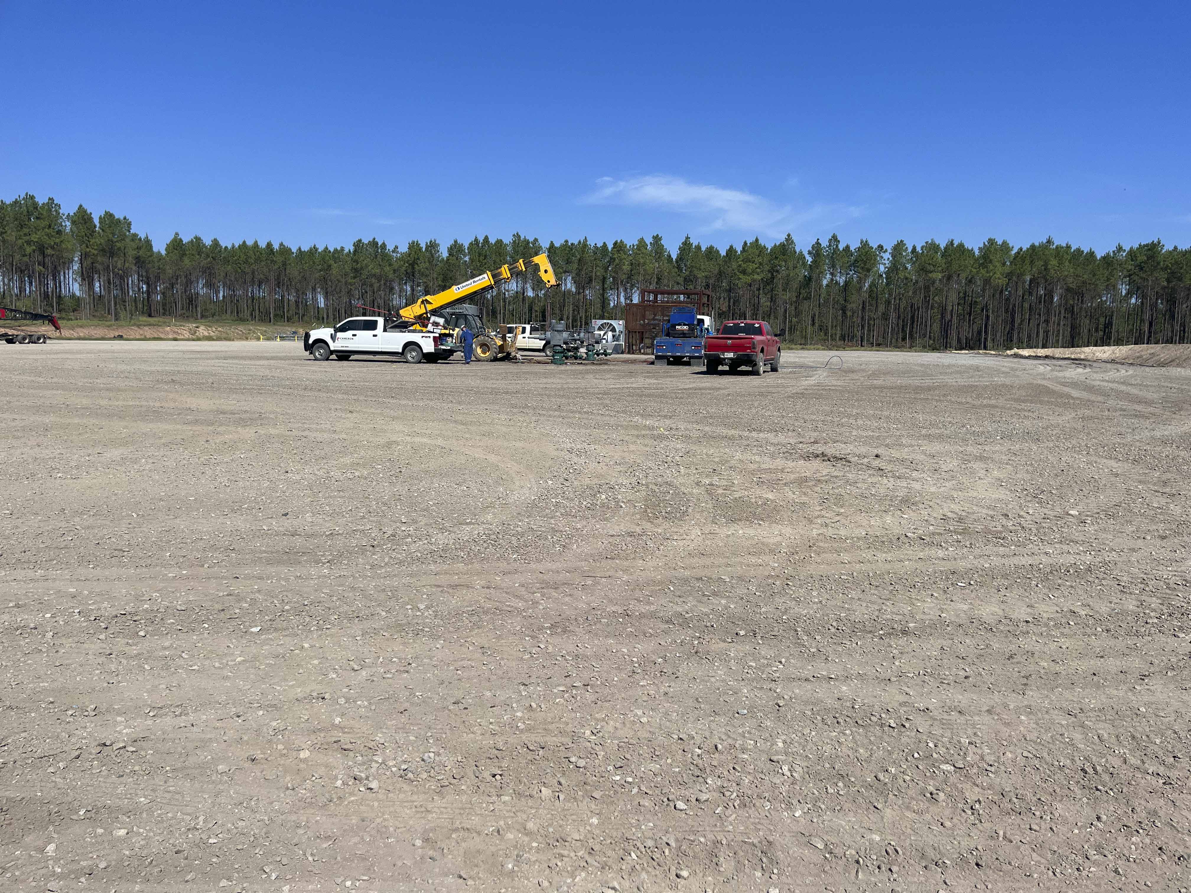 Oilfield laydown yard with trucks, telehandler, and equipment on prepared gravel pad