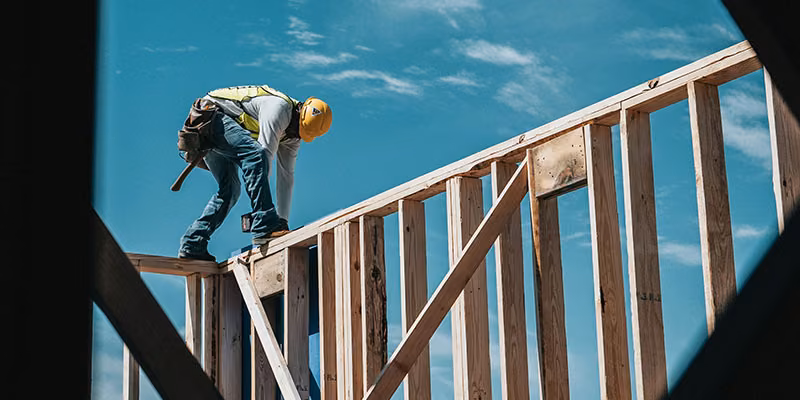 A construction worker standing on top of wooden building framework