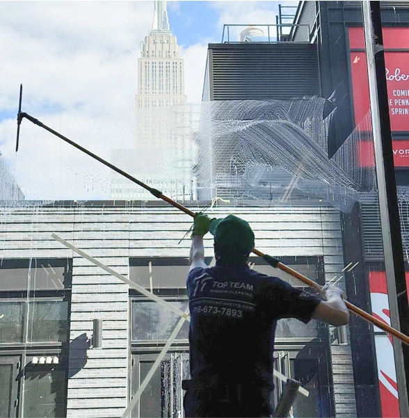 A window cleaner using a long squeegee to clean a large glass surface with the Empire State Building visible in the background.