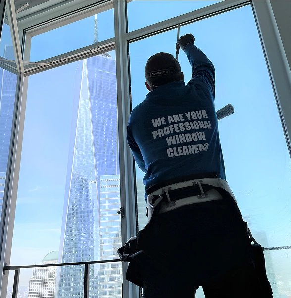 Window cleaner in uniform washing a tall glass window with an urban skyline visible outside.
