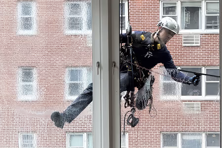 Window cleaner wearing a helmet and safety harness cleaning a building's exterior glass.