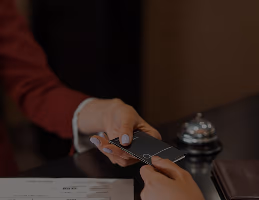 Hands exchanging a hotel key card over a reception desk with a service bell nearby.