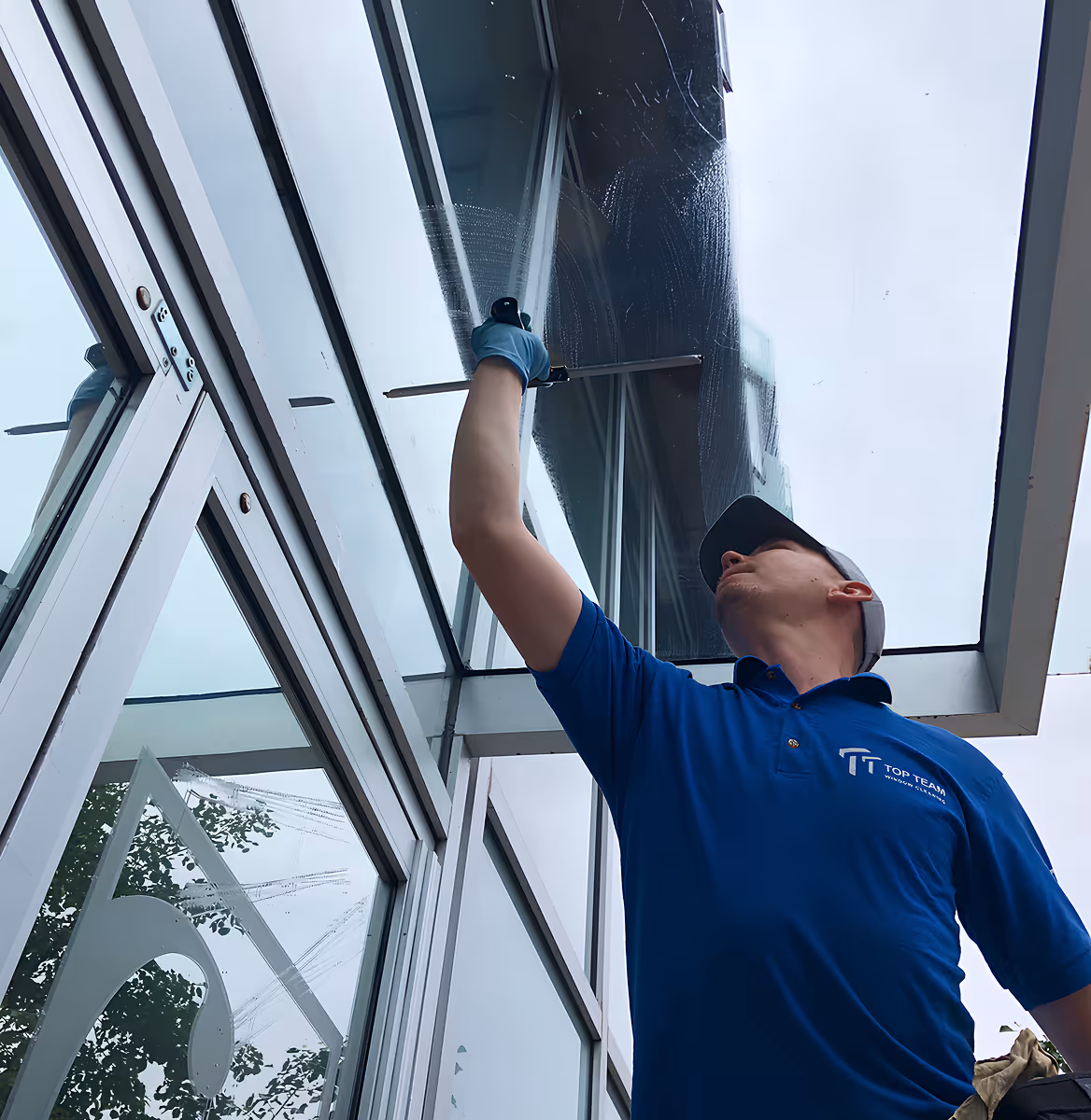 Person in blue shirt and cap cleaning a glass window with a squeegee outdoors.