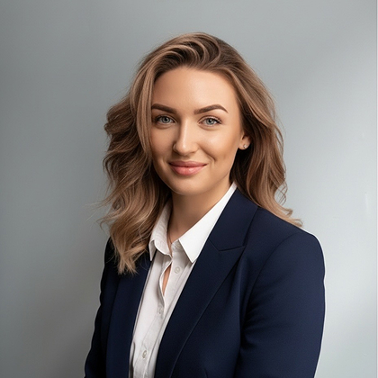 Smiling woman with wavy hair wearing a navy blazer and white shirt against a gray background.