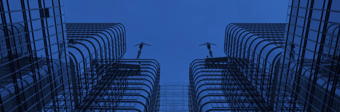Looking up at modern glass skyscrapers with cranes against a clear blue sky.