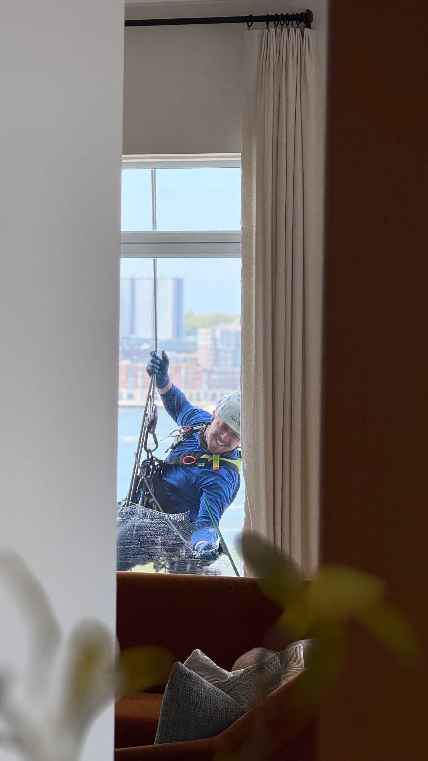 Window cleaner in safety gear cleaning an exterior window while suspended outside a building.