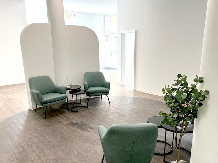 Modernes Wartezimmer mit drei grünen Sesseln, zwei schwarzen Beistelltischen und einer grünen Zimmerpflanze vor weißen Wänden.