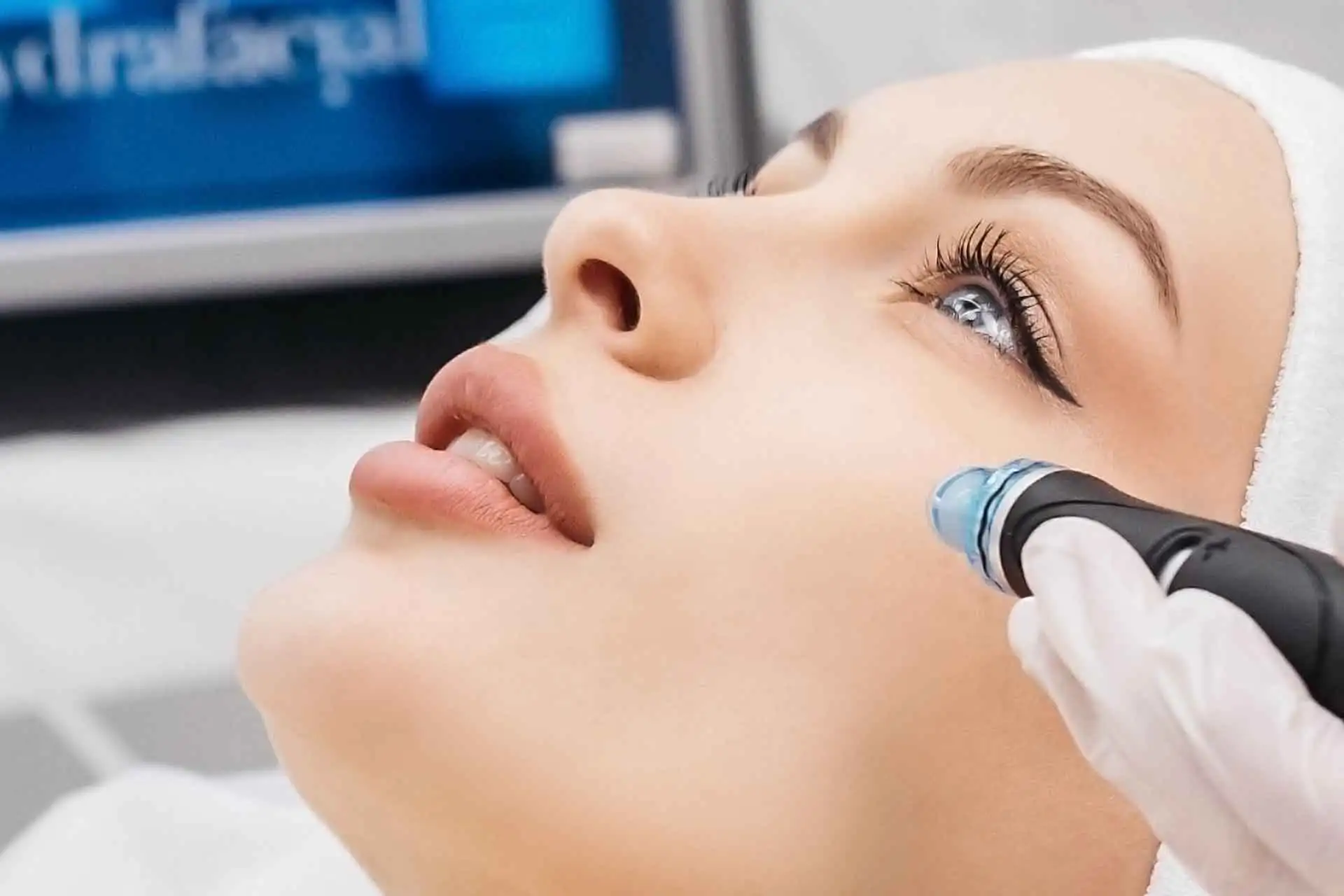 Frau erhält eine HydraFacial-Behandlung an der Wange mit einem blauen Handgerät.