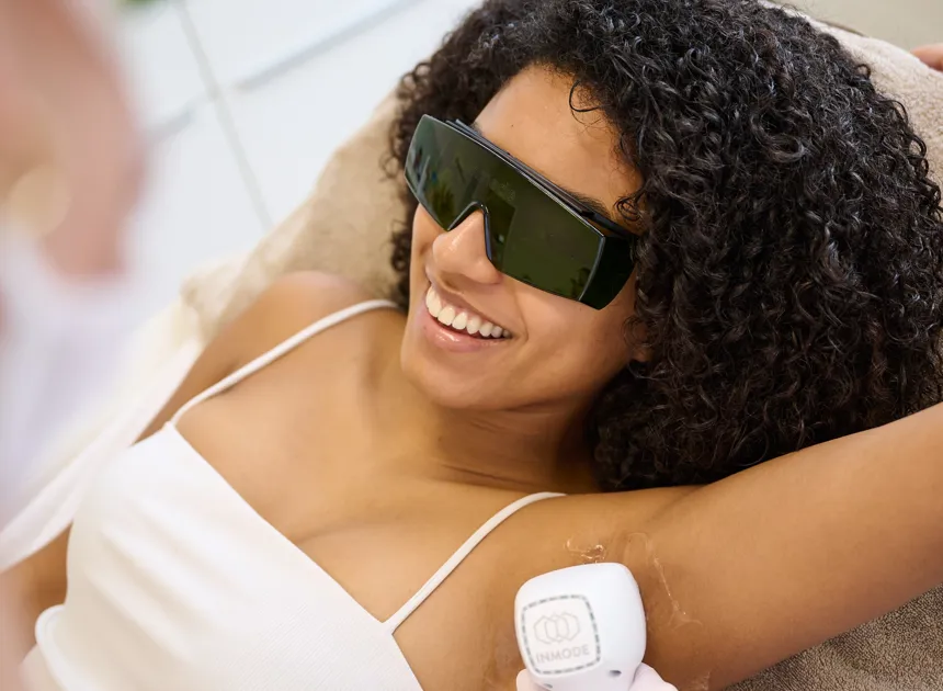 Frau mit lockigem Haar trägt Schutzbrille und erhält Laser-Haarentfernung an der Achselhöhle.