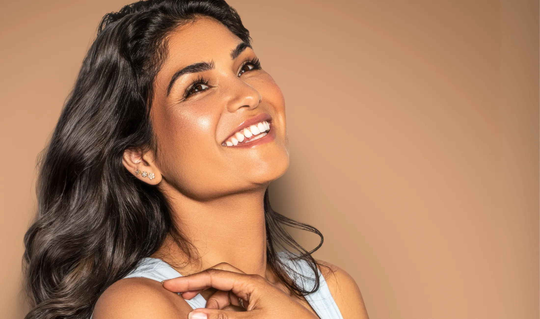 Lächende Frau mit langen dunklen Haaren vor beigefarbenem Hintergrund.