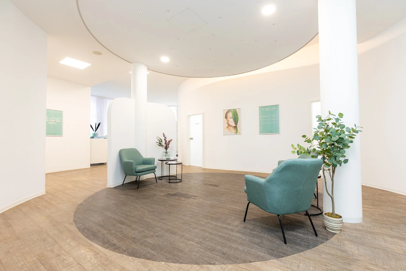 Heller moderner Wartebereich mit zwei grün-blauen Sesseln, kleinen Tischchen, einer Pflanze und weißen Wänden.