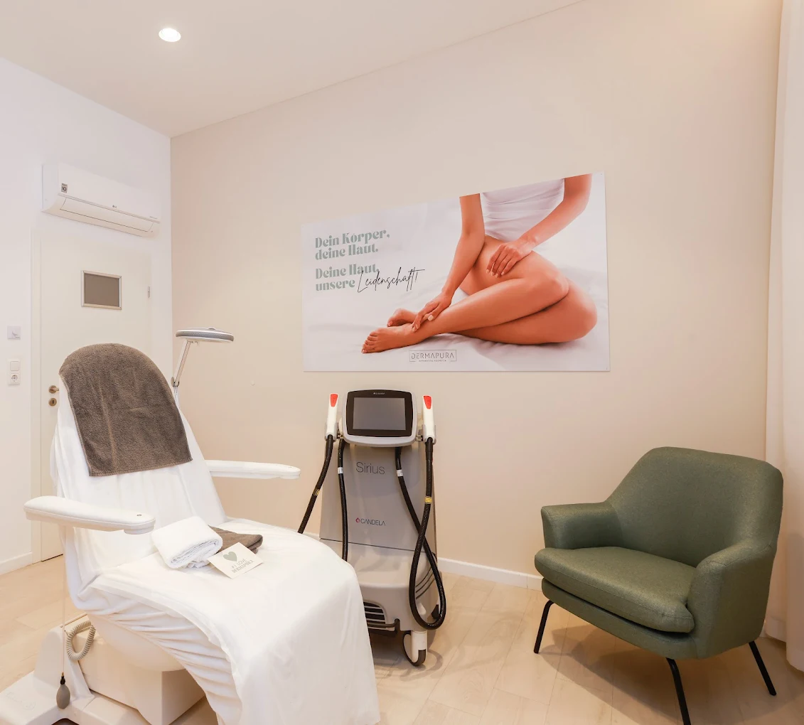 Behandlungsraum mit einer weißen Liege, einem Hautbehandlungsgerät, einem grünen Sessel und einem Wandplakat mit einem Bild von nackten Beinen.