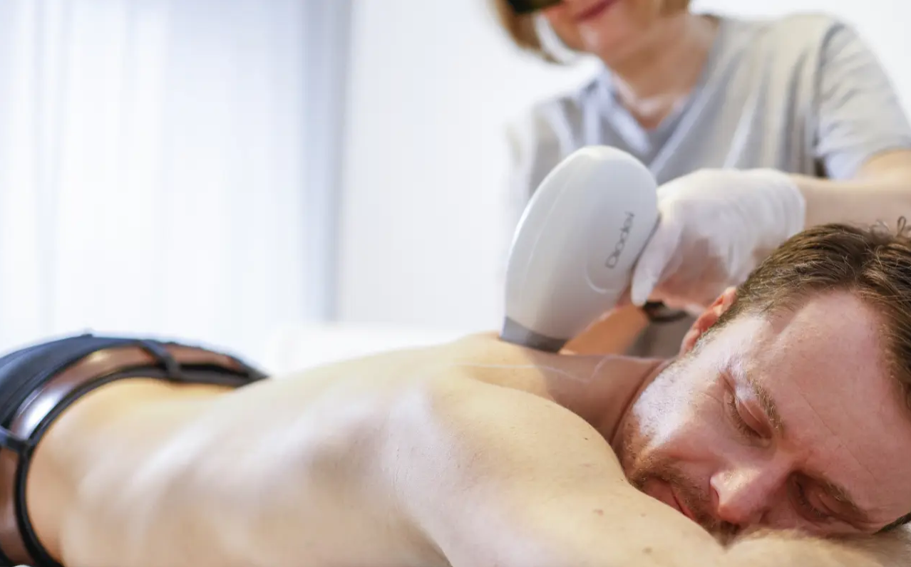 Mann liegt entspannt auf dem Bauch, während eine Kosmetikerin ihm mit einem Gerät die Rückenhaut behandelt.