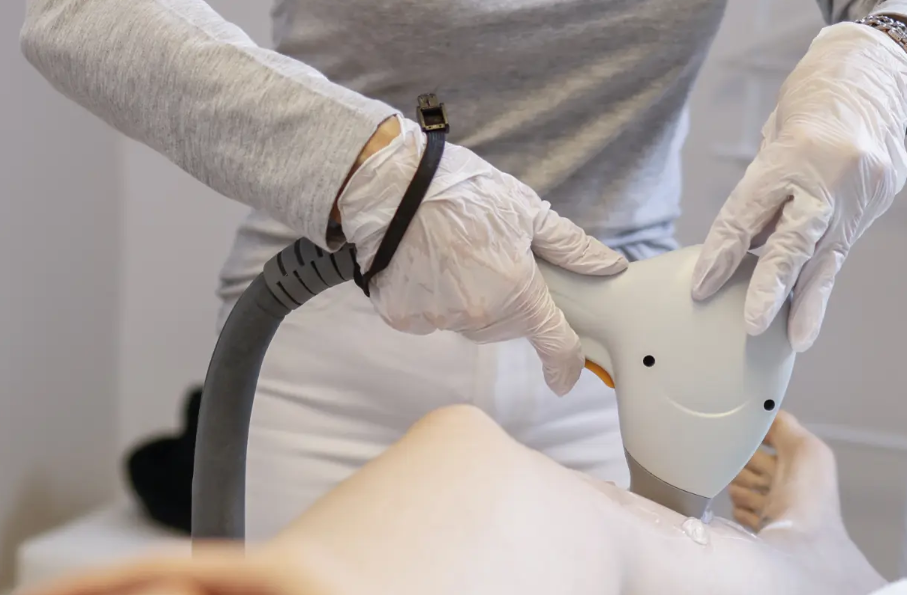 Person mit weißen Handschuhen, die ein medizinisches Gerät zur Laserbehandlung auf ein Bein hält.