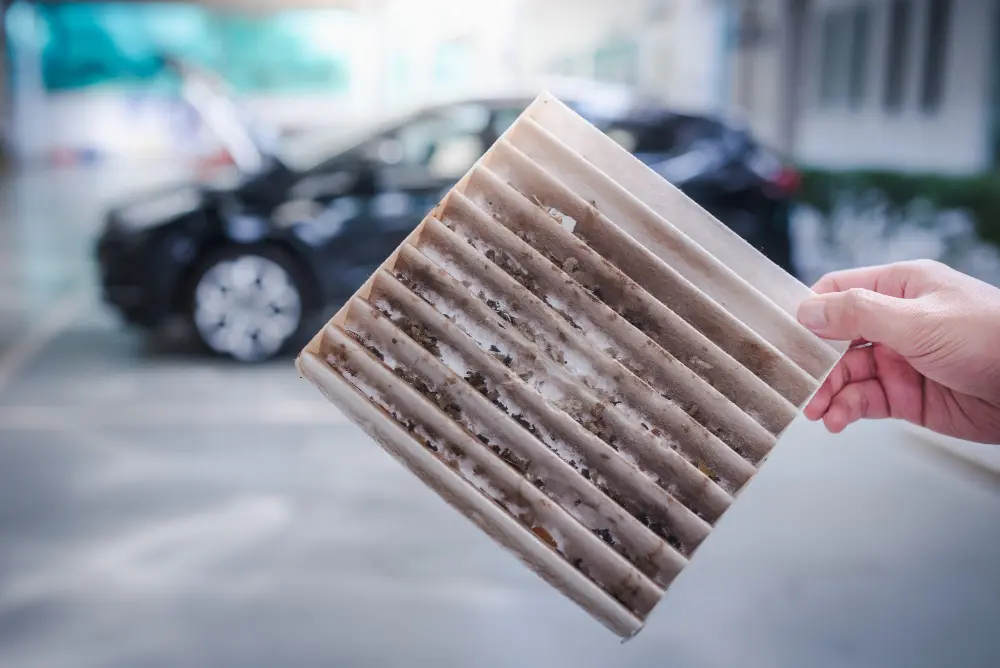 A hand holding a dirty cabin air filter