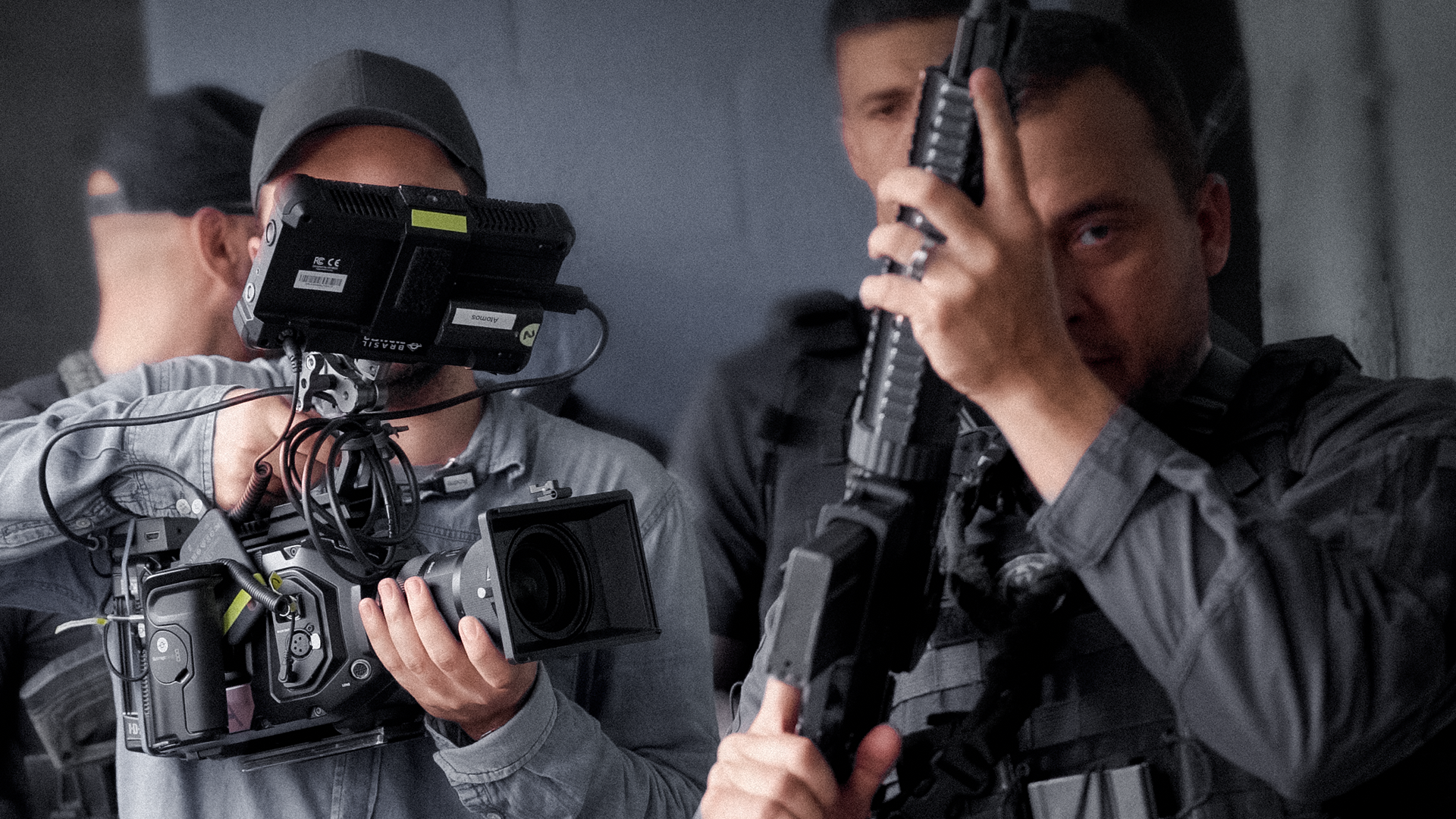 Imagem de bastidores da gravação do documentário 'Entre Lobos' da Brasil Paralelo com um policial segurando um fuzil e um cinegrafista segurando uma câmera