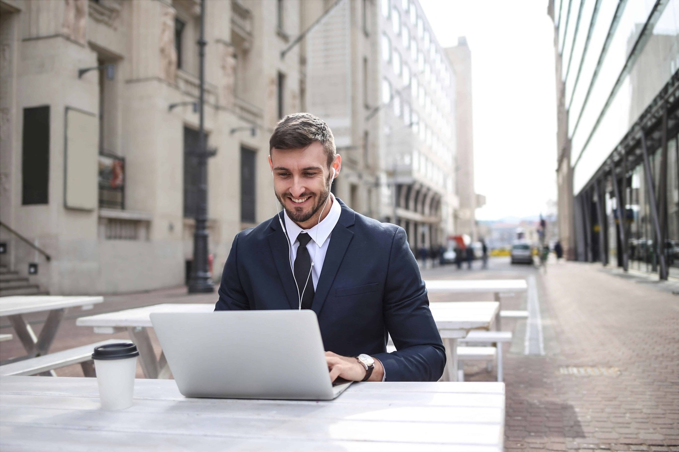 Smiling business owner working on a laptop on a table in a city square.