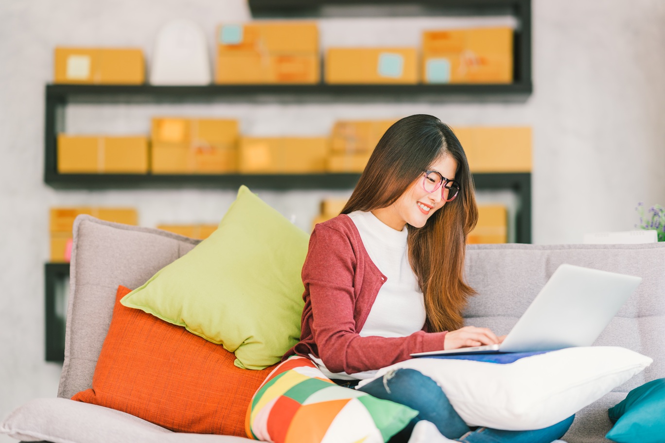 A small business owner sitting on a sofa and smiling while working on her laptop.
