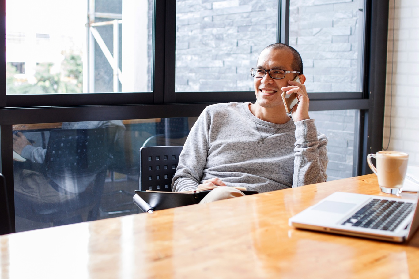 Small business owner sitting at a desk with his laptop taking a phone call.